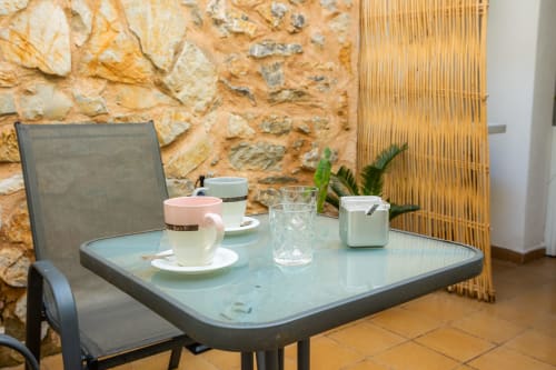 Zona de estar en la terraza del Apartamento Jaume B en Artà con muros de piedra, mesa servida con tazas de café y vasos