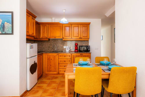 Luminosa zona de cocina-comedor en Apartamento Jaume B, Artà con muebles de madera, lámpara colgante azul y sillas amarillas en la mesa