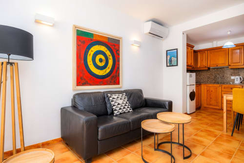 Sala moderna en Apartamento Jaume B, Artà con sofá de cuero negro, mesillas de madera, arte colorido y espacio abierto