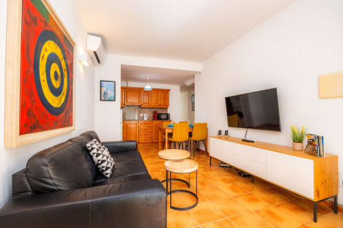 Moderno salón en Apartamento Jaume B, Artà con sofá de piel negra, TV de pantalla plana, muebles de madera y cocina abierta