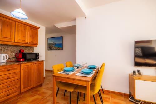 Comedor luminoso con mesa de madera, sillas amarillas y cocina equipada en Apartamento Jaume B, Artà