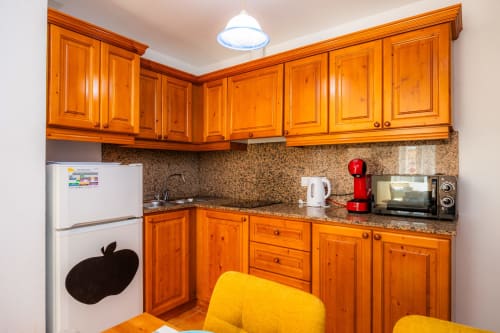 Cocina moderna con armarios de madera, encimera de granito y silla amarilla en Apartamento Jaume B, Artà