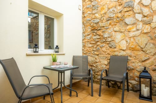Zona de estar en el patio del Apartamento Jaume B en Artà con muros de piedra, sillas, mesa y ventana
