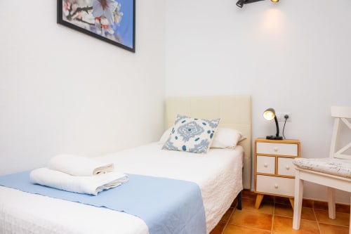 Dormitorio luminoso en Apartamento Jaume B, Artà con cama de cabecero crema, manta azul, mesita de noche de madera y escritorio blanco.