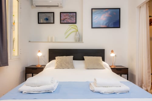Dormitorio luminoso en Apartamento Jaume B, Artà con ropa de cama blanca, cabecero oscuro, cuadros, TV de pared y ambiente acogedor