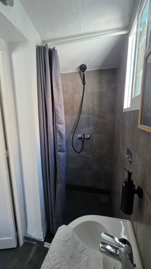 Modern shower stall with dark tile walls and handheld showerhead at Casa de Océano hotel in Tarifa