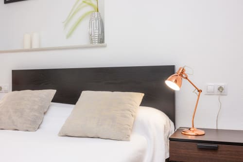 Dormitorio moderno en Apartamento Jaume B, Artà con cabecero oscuro, almohadas beige, lámpara de cobre y ropa de cama blanca
