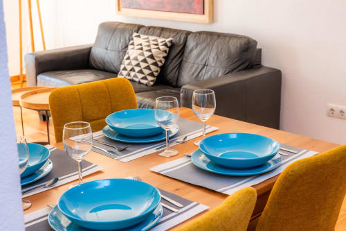 Comedor del Apartamento Jaume B en Artà con cubertería azul, sillas amarillas y sofá de cuero oscuro.