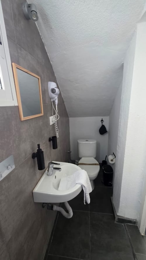 Compact bathroom in Ostro room at Casa de Océano, Tarifa with white sink, toilet, and black tiled floor
