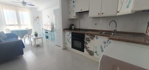 Bright kitchen-living area in El Médano apartment with white cabinetry, sea views from balcony, and modern amenities