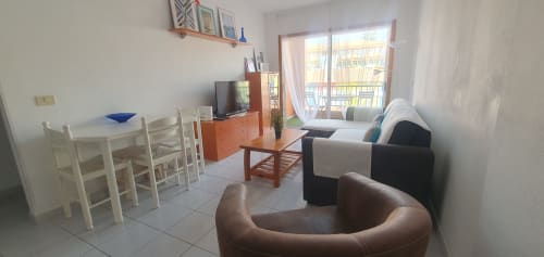 Bright apartment living room in El Médano with dining table, sofa, TV, wooden furniture and balcony overlooking city