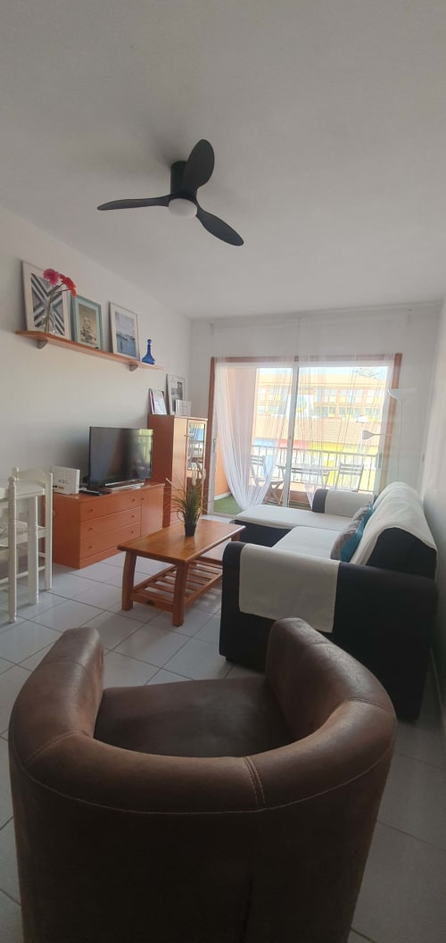 Modern apartment living room in El Médano with seating, TV, wooden furniture, ceiling fan, and sea view balcony
