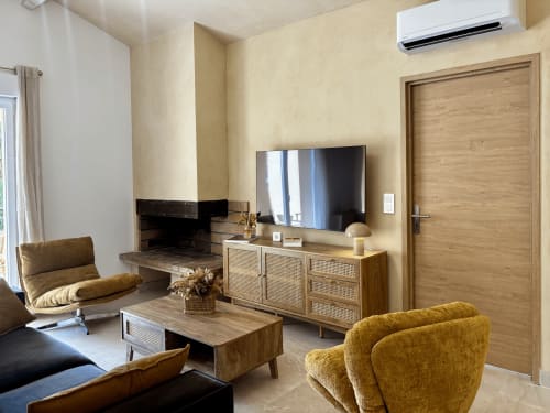 Salon moderne de la villa Casa Loc Conciercerie à Calenzana avec cheminée, télévision murale, mobilier en rotin et finitions en bois