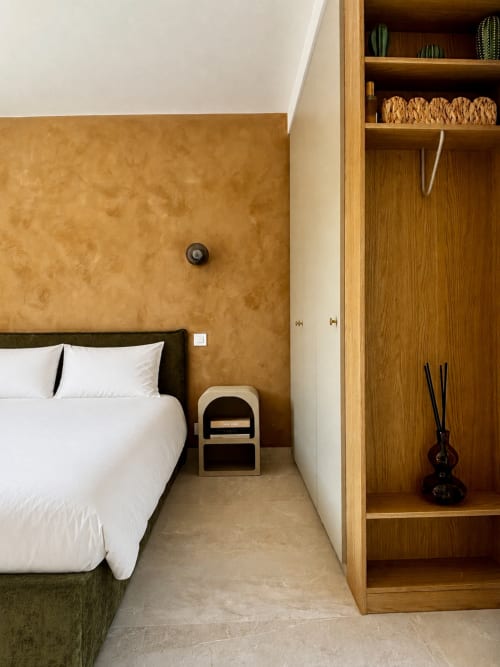 Chambre minimaliste à Casa Loc Conciergerie avec mur ocre, literie blanche, étagères en bois et vue montagne