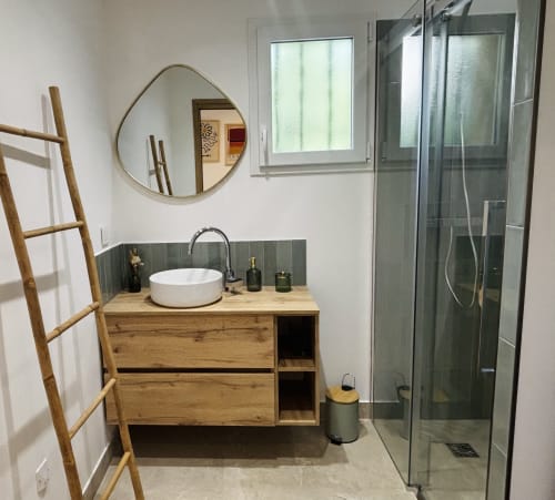Salle de bains contemporaine de la villa Casa Loc Calenzana avec meuble-lavabo en bois, miroir rond, lavabo blanc et douche à l'italienne