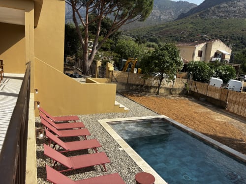 Villa Casa Loc à Calenzana avec piscine, transats rouges, bâtiment jaune et vue sur les montagnes en Corse