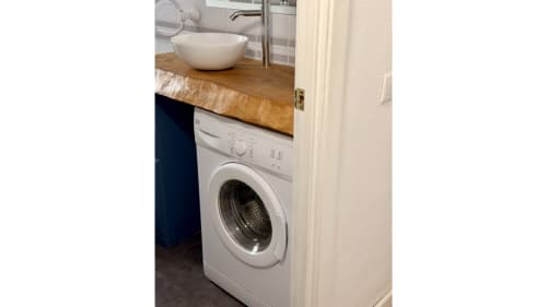 Baño compacto con lavadora bajo encimera de madera y lavamanos blanco de cerámica en apartamento Holidays Costa Brava