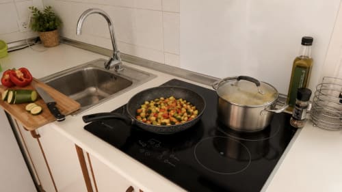 Moderna cocina en Holidays Costa Brava con placa de inducción, menaje, verduras frescas y fregadero de acero inoxidable