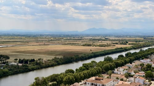 Vista panorámica desde Holidays Costa Brava en Empuriabrava: río, llanuras agrícolas y montañas lejanas bajo cielo nublado.