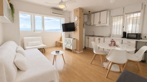 Luminoso apartamento moderno en Holidays Costa Brava con salón abierto, cocina, vistas panorámicas a la ciudad, mobiliario blanco y