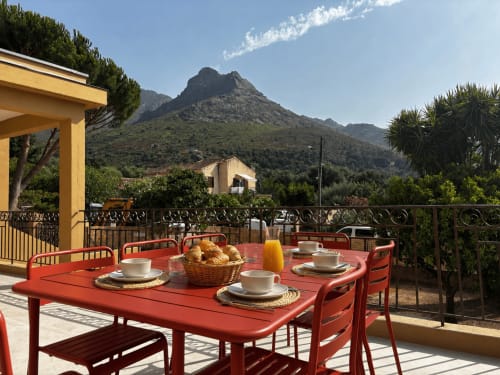 Table à manger rouge dressée pour le petit-déjeuner sur la terrasse d'une villa avec vue sur les montagnes à Calenzana, Corse