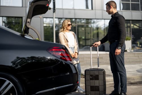 Casal com bagagens na entrada do hotel AgapeStay Porto, carregando mala do carro preto