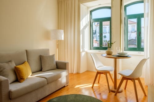 Apartamento luminoso em Porto na AgapeStay com sofá bege, mesa redonda, cadeiras brancas e janelas com moldura verde com vista para o histórico