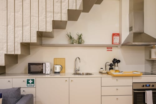 Cozinha compacta moderna na AgapeStay Porto com micro-ondas, chaleira, pia e fogão em design minimalista bege
