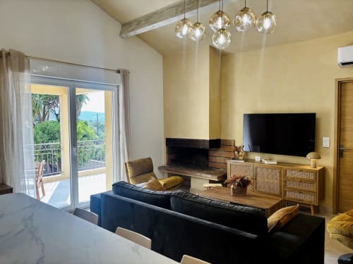 Salon contemporain à Calenzana : canapé noir, cheminée, vues montagnardes, luminaires suspendus et accès balcon