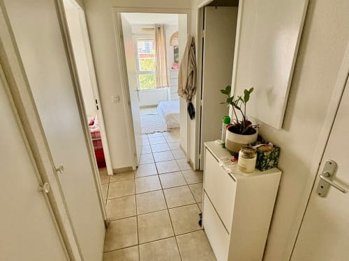 Couloir lumineux d'un appartement à Aix-en-Provence avec murs beige, carrelage, plante en pot sur étagère et portes ouvertes