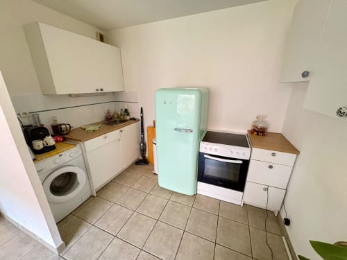 Cuisine moderne avec réfrigérateur menthe, four, lave-linge et meubles blancs dans un appartement d'Aix-en-Provence.