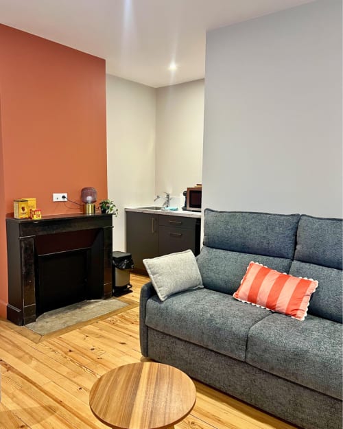 Salon moderne de Kipling House avec canapé gris, cheminée et mur d'accent orange, appartement à Saint Beauzire