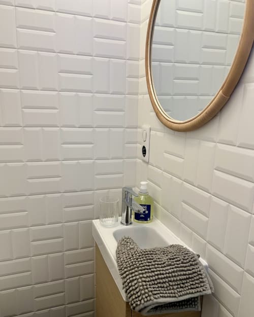 Salle de bain moderne dans l'appartement Kipling House avec carrelage métro blanc, miroir rond, lavabo avec accessoires et serviette texturée