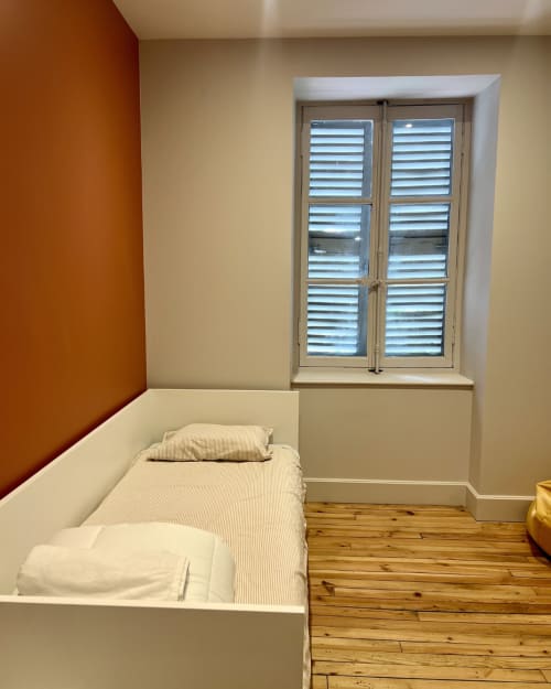 Chambre lumineuse à Kipling House avec lit simple, mur d'accent orange, parquet et fenêtre à volets à Saint Beauzire