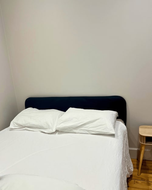 Chambre minimaliste du Château de Sampigny avec tête de lit sombre, draps blancs, table de nuit en bois et murs clairs
