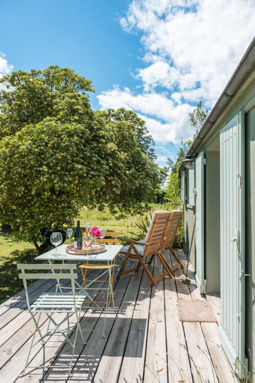 Terrasse en bois du gîte Le Cabanon avec table à manger, chaises et vue sur la verdure provençale sous un ciel bleu
