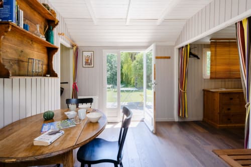 Salle à manger lumineuse avec table en bois, murs blancs et portes donnant sur le jardin à Locations Montjoïa Provence