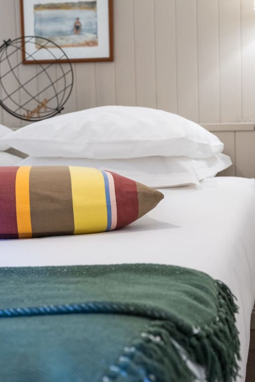 Coussin rayé coloré sur la literie blanche du gîte Le Cabanon, Locations Montjoïa Provence, Le Thor