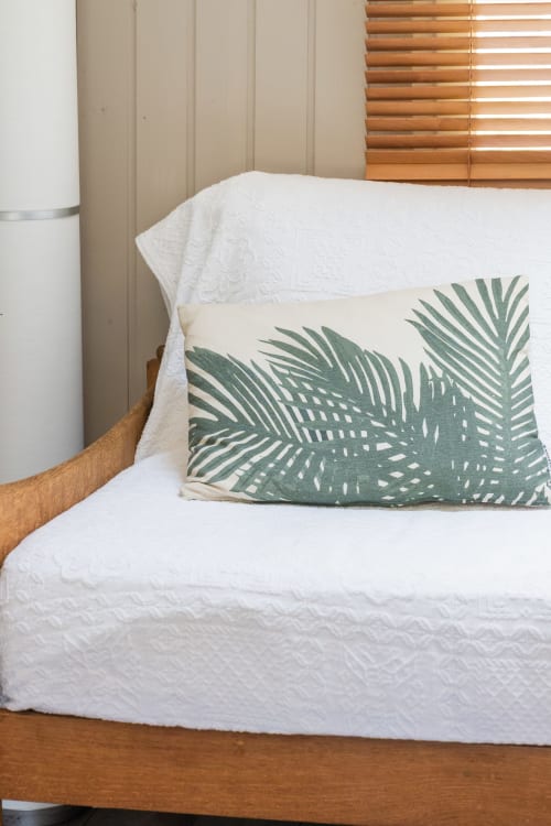 Lit aux draps matelassés blancs et coussin feuilles de palmier vert au gîte Le Cabanon en Provence, France