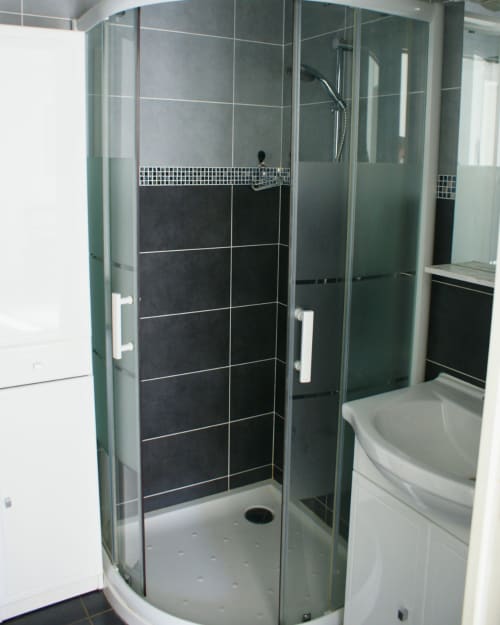 Douche moderne fermée aux murs en carrelage noir, portes vitrées et équipements blancs dans la salle de bain de l'appartement Kipling House