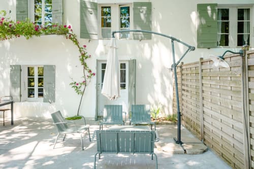 Cour ensoleillée de Locations Montjoía Provence avec sièges bleus, vignes fleuries, parasol blanc et clôture en bois