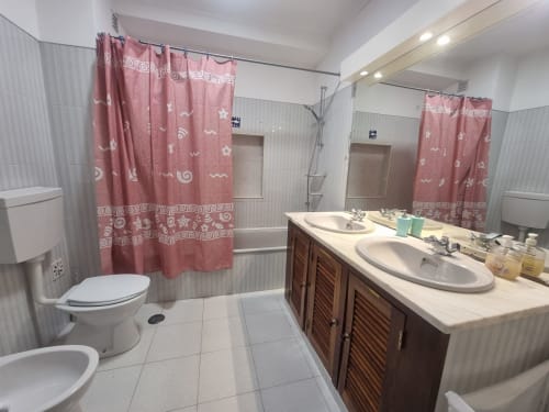 Banheiro espaçoso na Solazur By Ericeira Property com dupla pia, cortina de chuveiro bordô e acabamentos modernos