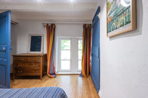 Chambre lumineuse aux piliers bleus, commode en bois, rideaux colorés et vue sur le jardin de la maison d'hôtes Le Gîte bleu en Provence