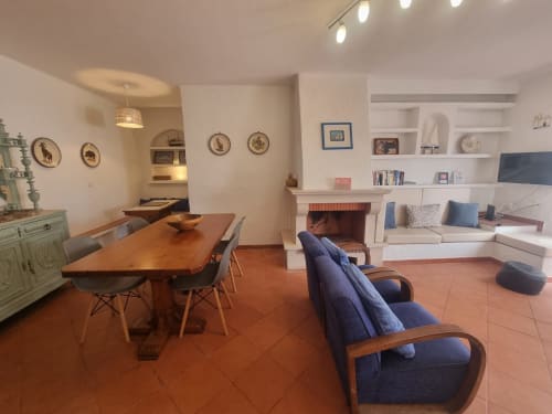 Sala de estar em plano aberto no Solazur By Ericeira com mesa de jantar em madeira, poltrona azul, lareira e móveis embutidos