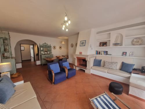 Sala de estar espaçosa em apartamento em Ericeira com poltronas azuis, lareira, prateleiras embutidas e piso em azulejo terracota