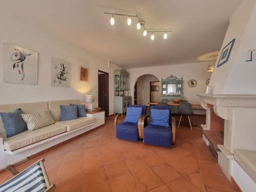Sala de estar espaçosa na Solazur By Ericeira com sofá creme, poltronas azuis, azulejos terracota, lareira e design moderno
