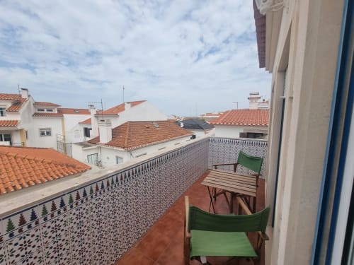 Terraço do Solazur Ericeira com cadeiras verdes, mesa de madeira e vista sobre os telhados da cidade em Portugal