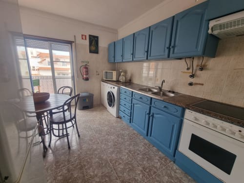 Cozinha azul e branca com área de refeições e máquina de lavar no apartamento Solazur, Ericeira Portugal