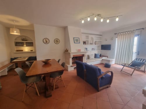 Espaçosa sala de estar do Solazur, Ericeira com mesa de jantar, poltrona azul, lareira e comodidades modernas