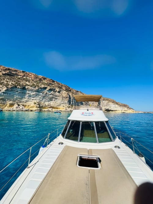 Motobarca bianca con ponte color sabbia sulle acque azzurre del Mediterraneo vicino alle scogliere rocciose di Lampedusa, Italia